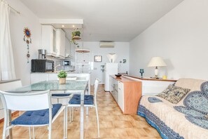 A compact living space with a kitchenette, a dining area with chairs, a sofa, and a small table with a lamp. - IBIZA BRAMER 11  Canyelles Roses (Rosas / Roses)