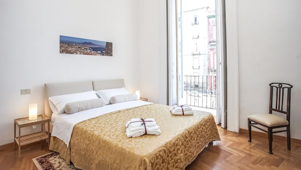 A neatly arranged bedroom with a bed, bedside tables, a chair, and a window with a cityscape view. - Neapolitan house, unique history and view (Napoli)