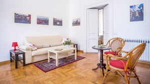 A living room with a sofa, a coffee table, a red lamp, wicker chairs, and a small table with a vase of flowers. - Neapolitan house, unique history and view (Napoli)