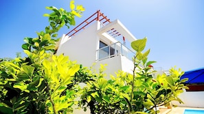 Um edifício moderno com fachada branca, estrutura metálica vermelha no telhado e céu azul límpido.
