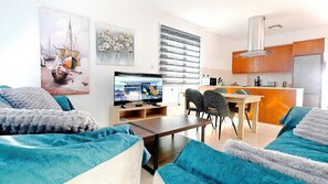 Uma sala de estar com televisão, canto de jantar e cozinha.