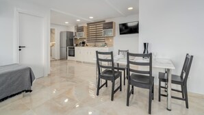 A modern kitchen with white cabinets, a dining table with four chairs, and a TV mounted on the wall. - Urban Loft with balcony across the Acropolis! (Athina)