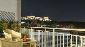 A balcony with wicker furniture, a red lantern, and a view of a historic building at night. - Urban Loft with balcony across the Acropolis! (Athina)