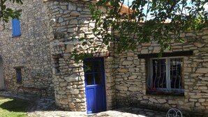 A stone building with a blue door and window, a round metal table, and a bench.