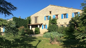 A stone house with blue shutters, surrounded by lush greenery and a well-maintained lawn.