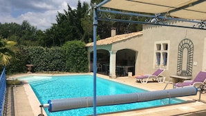 A swimming pool with a pergola, lounge chairs, and a covered patio area.