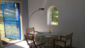 A dining area with a table set for four, a chair, a floor lamp, and a window with a view of greenery.