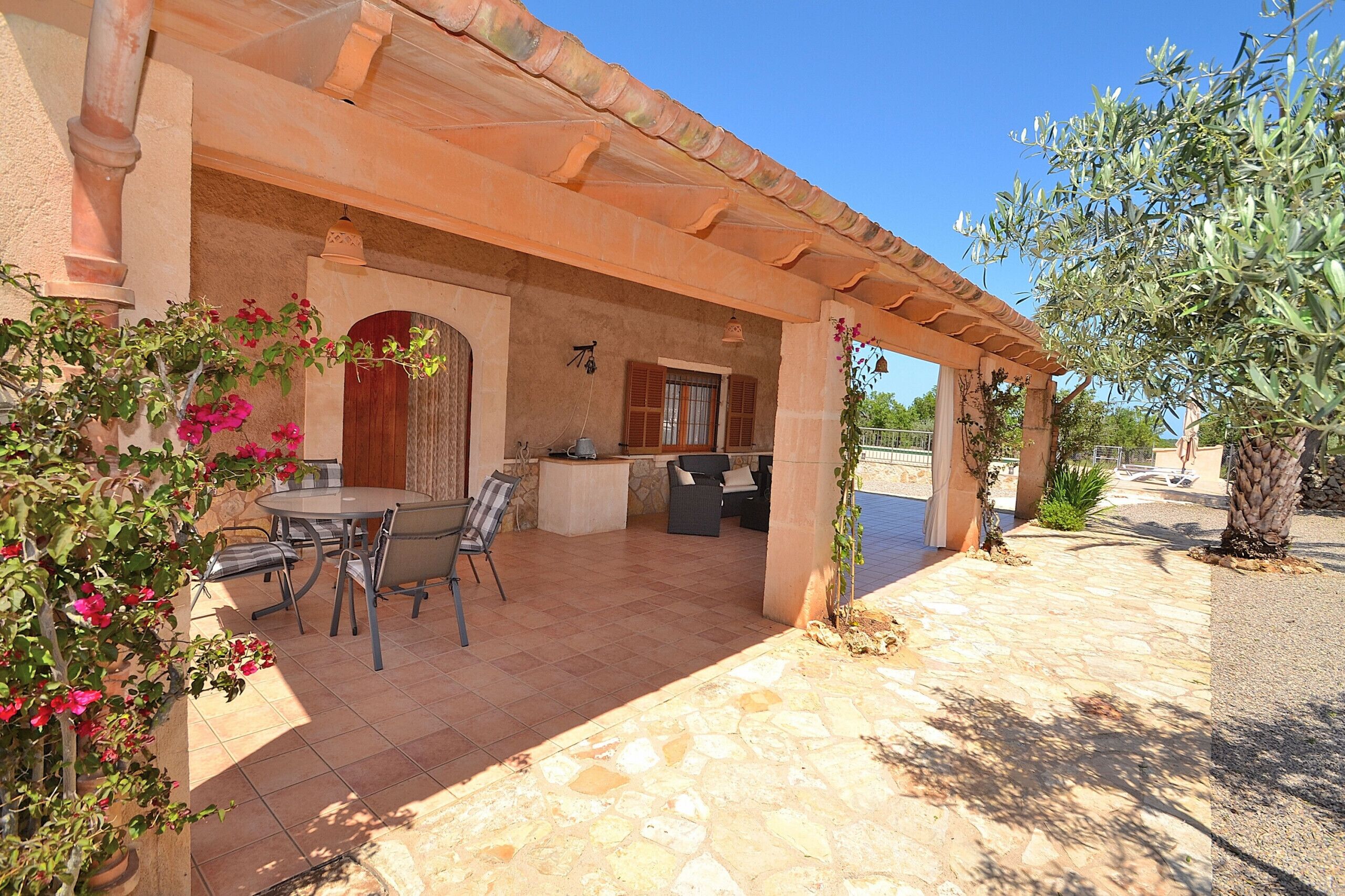 A covered patio area with a round table and chairs, a kitchen area, and a stone-tiled floor.