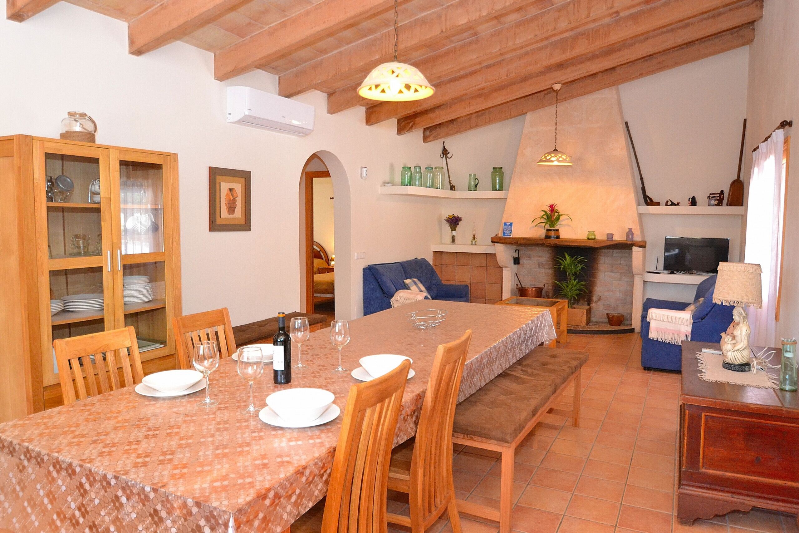 A dining area with a table set for four, wooden chairs, a bench, and a fireplace with a TV.