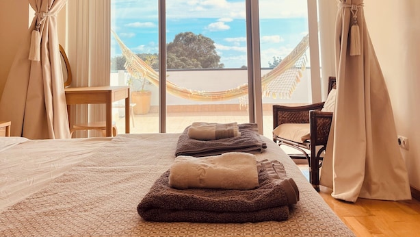 A hotel room with a large bed, a view of the sea, and a hammock outside.