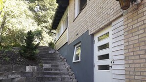 A residential building with a stone staircase leading to a door, surrounded by a brick wall and a small garden area. - Partille Homestay. 4 rooms with kitchen. (Partille)