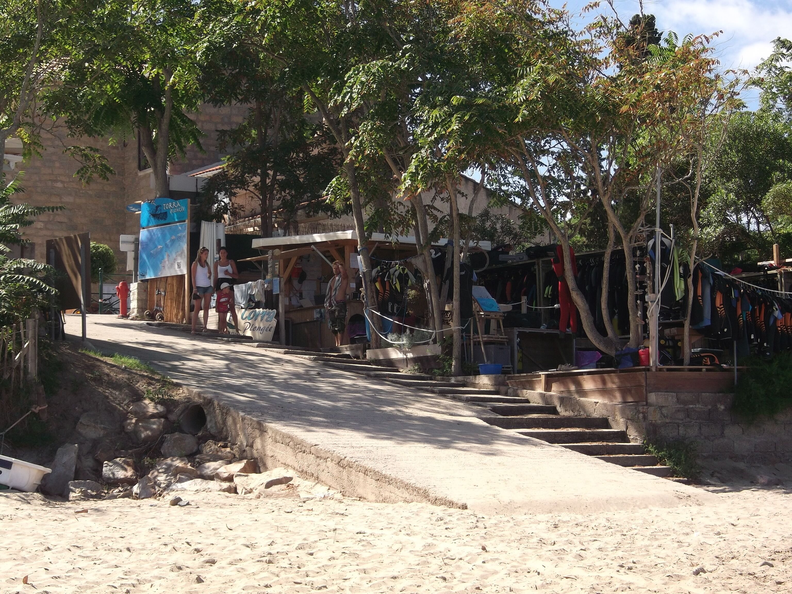 Una calle frente a la playa con una pequeña tienda y un letrero que dice "TOKRA PLONGÉE".