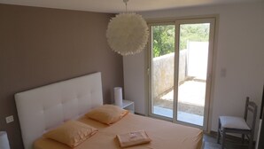 Ein Schlafzimmer mit Bett, Kissen, Nachttisch, Stuhl und Blick ins Freie.