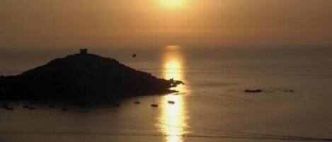 Un coucher de soleil sur une mer calme, avec une petite île et des bateaux.