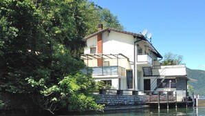 Ein zweistöckiges Haus mit Balkon, einer Steinmauer und einem Steg, der ins Wasser führt.