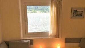 Ein Zimmer mit einem Bett, zwei Nachttischen mit Lampen, einem Fenster mit Blick auf ein Gewässer und einem gerahmten Bild an der Wand.