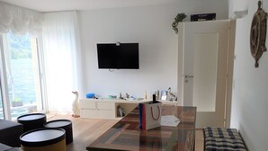Ein Wohnzimmer mit Holztisch, einer Couch, einem Fernseher und Blick ins Freie.