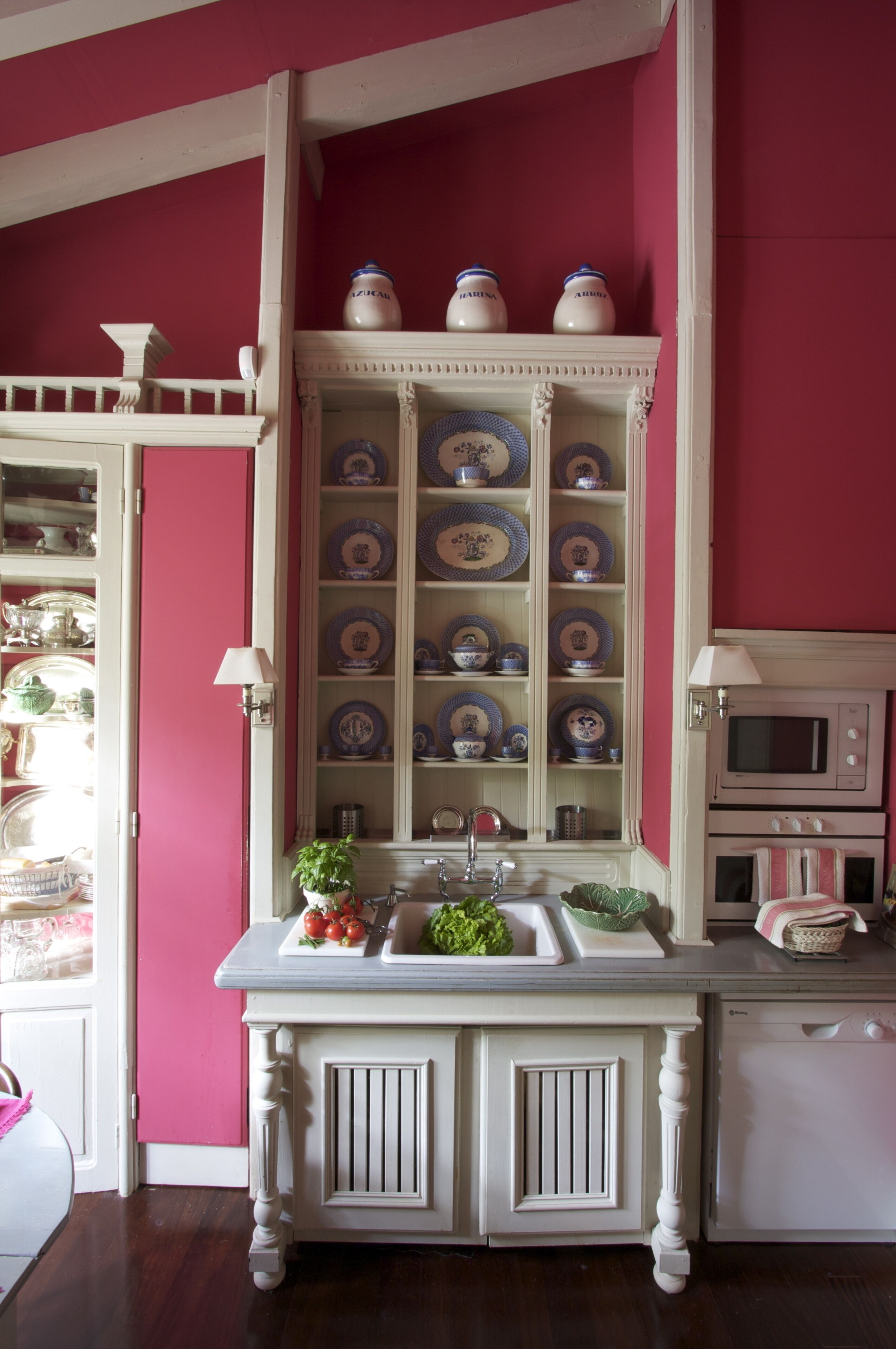 A kitchen with a pink wall, white cabinetry, and a built-in oven.