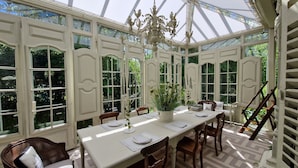 Ein Wintergarten mit Esstisch, umgeben von Stühlen und einer großen Topfpflanze.
