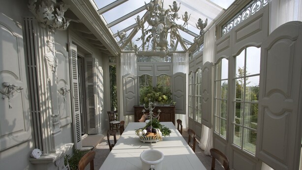 Ein Wintergarten mit Esstisch, Stühlen und einer Deckenleuchte.