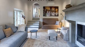 Una sala de estar con chimenea, un sofá, un reposapiés estampado y una pequeña mesa redonda.