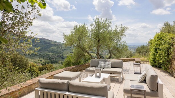 Un espacio al aire libre con sofás y mesas, con vistas a un paisaje escénico de árboles y colinas distantes.