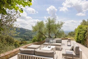 Een terras met banken en tafels, met uitzicht op een aantrekkelijk landschap met bomen en heuvels in de verte.