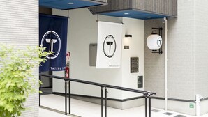 A modern building entrance with a blue banner, a white sign, and a hanging light fixture. - Trip Pod Takasago A (Fukuoka)