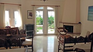 A living room with a fireplace, a television, and a dining area with wooden furniture. - villa anthousa  with excellent view (ANTHUSA)