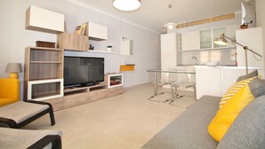 A modern living room with a flat-screen TV, a glass dining table, and a sofa with striped cushions.