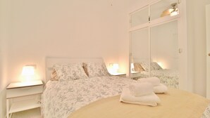 A neatly made bed with floral bedding and a beige comforter, two bedside lamps, a white nightstand, and a large mirror above the bed.