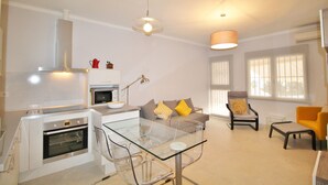 A modern kitchen with a built-in oven and microwave, a glass dining table, and a seating area with a sofa and armchairs.