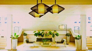 Un hall d’entrée avec un ensemble de canapés, deux plantes en pot et des lampes suspendues.