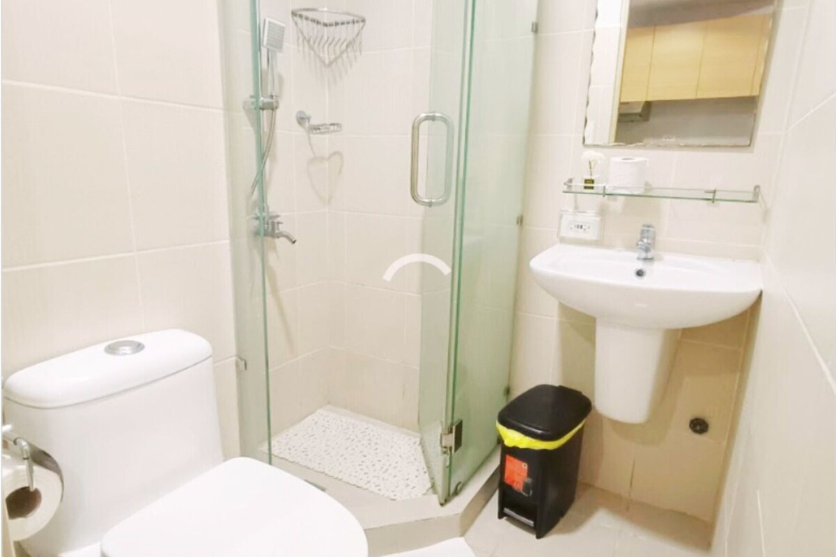 Un baño moderno con ducha envuelta en vidrio, un inodoro blanco y un lavamanos con espejo superior.