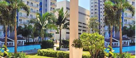A modern residential building with multiple balconies, a swimming pool, and lush greenery.