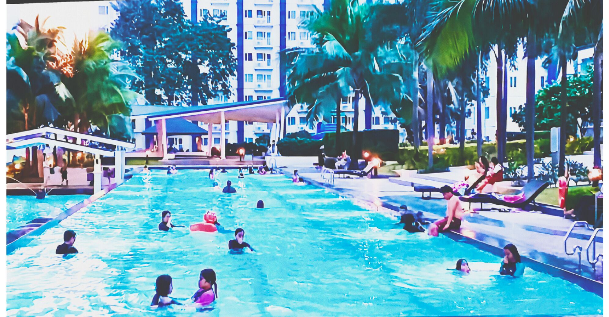 A swimming pool with multiple lanes, surrounded by palm trees and a covered area with seating.