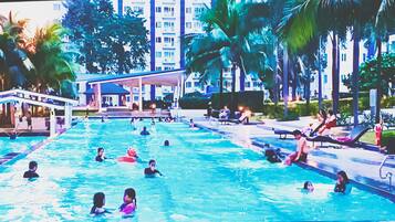 A swimming pool with multiple lanes, surrounded by palm trees and a covered area with seating.