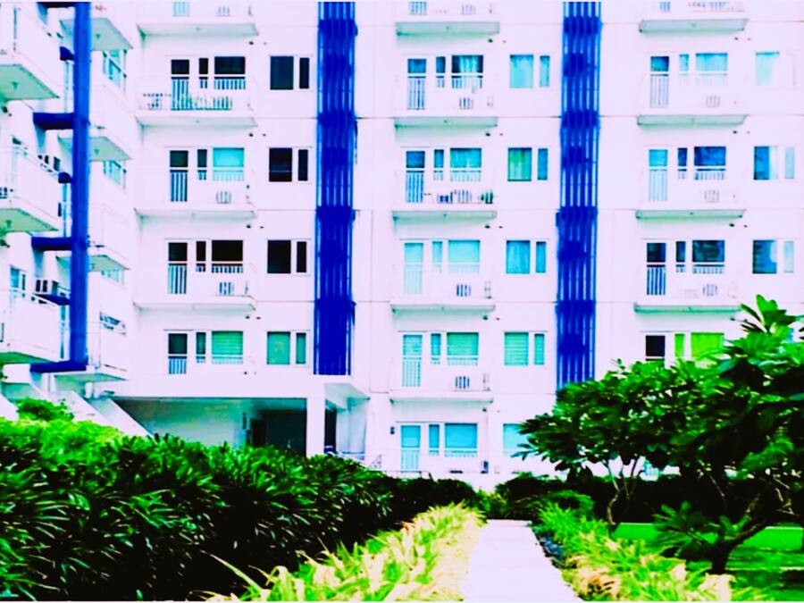 Un edificio residencial de varios pisos con balcones, un camino central y follaje circundante.