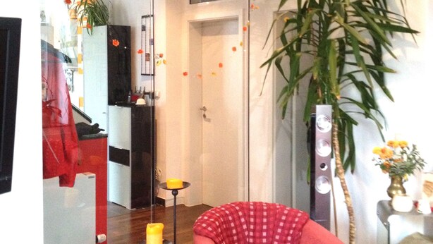 A living room with a red armchair, a large mirror reflecting the room, a potted plant, and a small table with a candle. - Duplex apartment in Südstadtvilla (Eisenach)