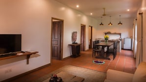 A modern living room with a flat-screen TV, a wooden coffee table, and a sofa. There is a dining area with a table and chairs, and a kitchen in the background. - The Orientation Lodge (Siem Reap)