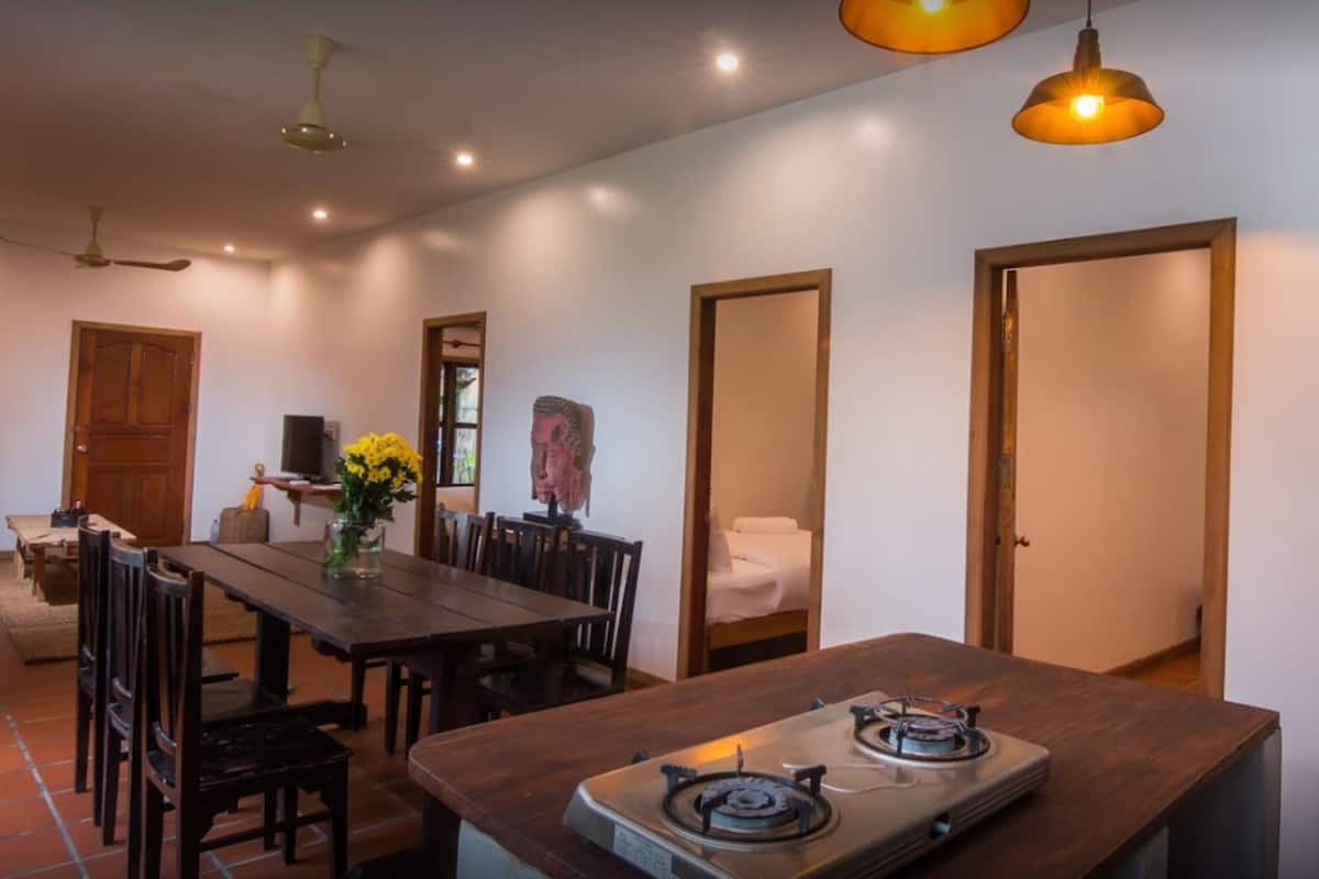 A dining area with a wooden table, chairs, and a gas stove. There are ceiling lights and a door leading to another room.