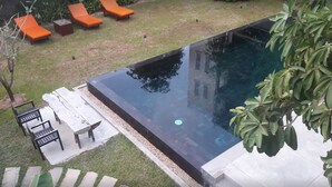 A swimming pool with a clear view of the water, surrounded by a grassy area with lounge chairs and a table. - The Orientation Lodge (Siem Reap)