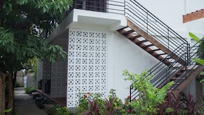 A modern building with a white exterior, a wooden staircase with a metal railing, and a patterned wall. - The Orientation Lodge (Siem Reap)