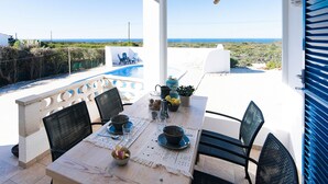 A dining area with a table set for two, overlooking a pool and the sea.