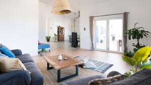 A modern living room with a sofa, a coffee table, and a dining area in the background.
