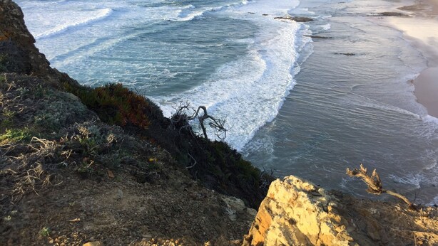 A coastal landscape with a rocky shoreline and waves crashing onto the beach.