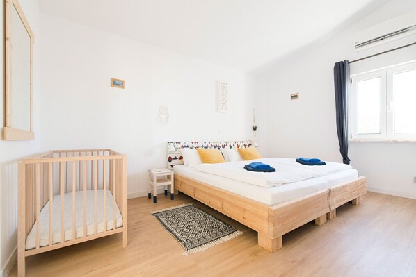 A bedroom with a wooden crib, a single bed with a headboard, a nightstand, and a small table.