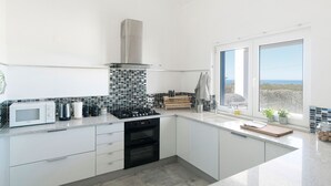 A modern kitchen with white cabinets, a black stove, a microwave, and a view of the ocean through a large window.