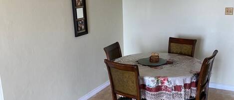 Un comedor con una mesa redonda, cuatro sillas, una araña y un cuadro en la pared.