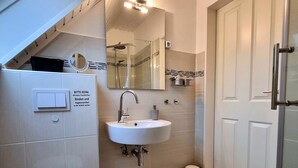A bathroom with a white sink, toilet, and a mirror. There is a shower visible in the reflection. - **** classified comfort vacation apartment 300 m to the beach, incl. beach chair  (Grömitz)